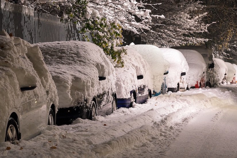 Line of multiple cars parked up covered in layers of heavy snow