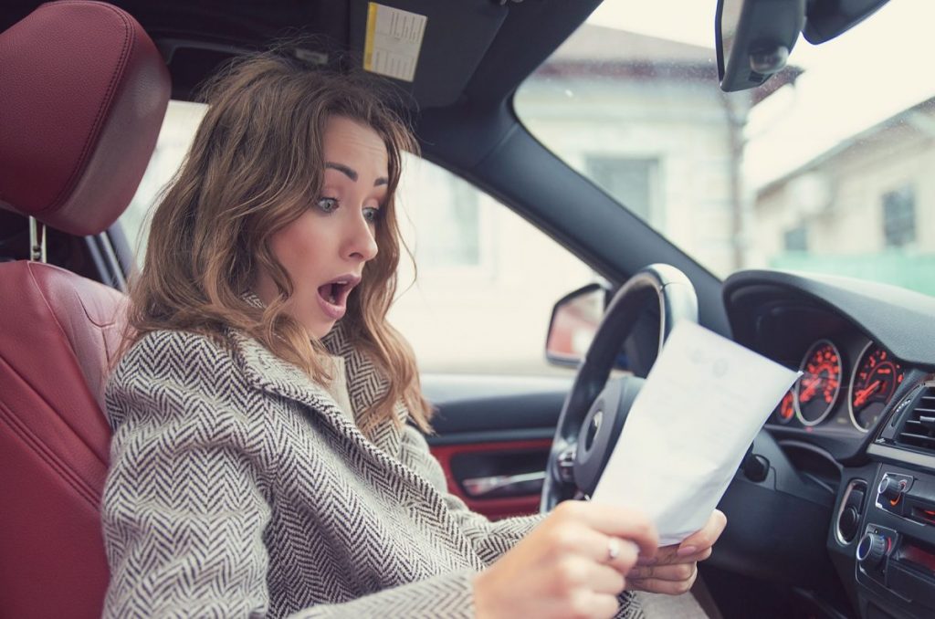 Women sitting on red leather seat in a car with a shocked expression while holding their MOT advisory note