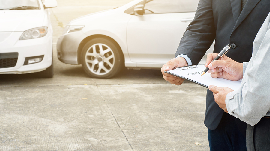 Two people standing beside each other, both holding onto the same clipboard showing information with cars parked behind