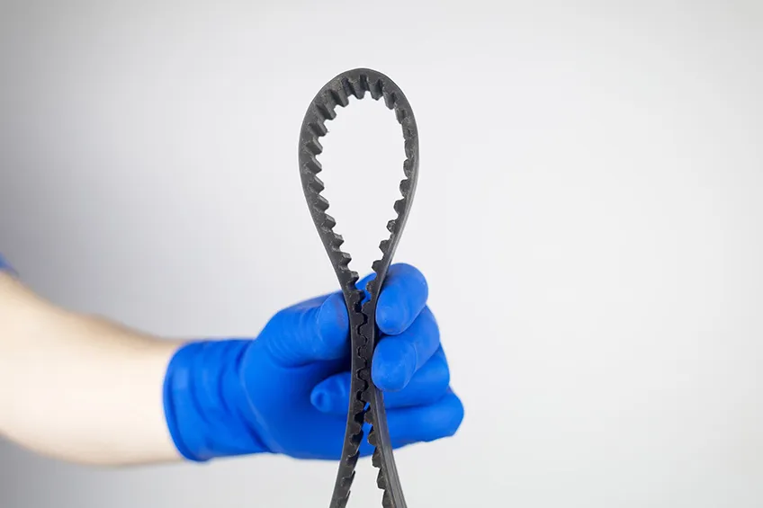 A gloved mechanic holds a worn rubber cambelt that has been replaced.